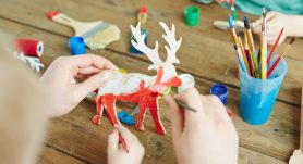Hands of adult and kid painting wooden deer in red