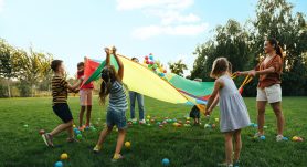 Group,Of,Children,And,Teacher,Playing,With,Rainbow,Playground,Parachute